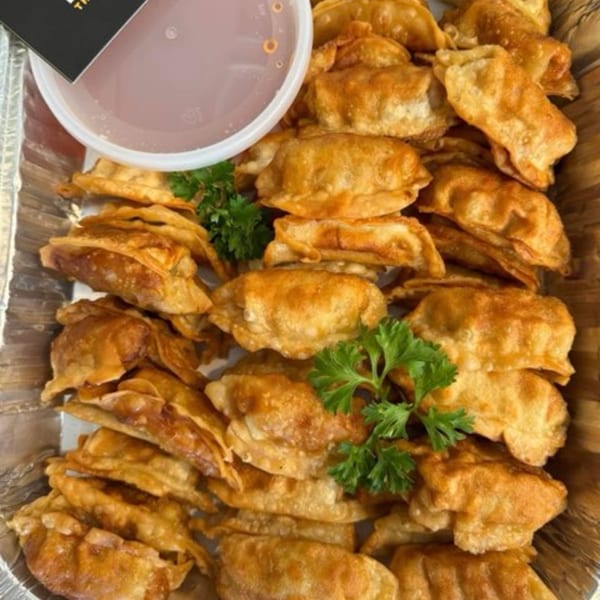 Crispy fried Thai dumplings with fresh parsley in a foil tray, with a side of dipping sauce.