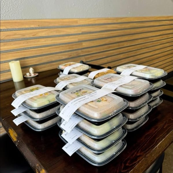Stacks of Delish Thai Kitchen takeout containers with labels on a wooden table.