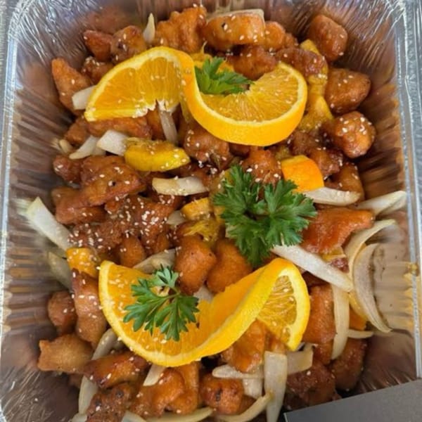 Delish Thai Kitchen's orange chicken with sesame seeds, onions, orange slices, and parsley in a foil container.