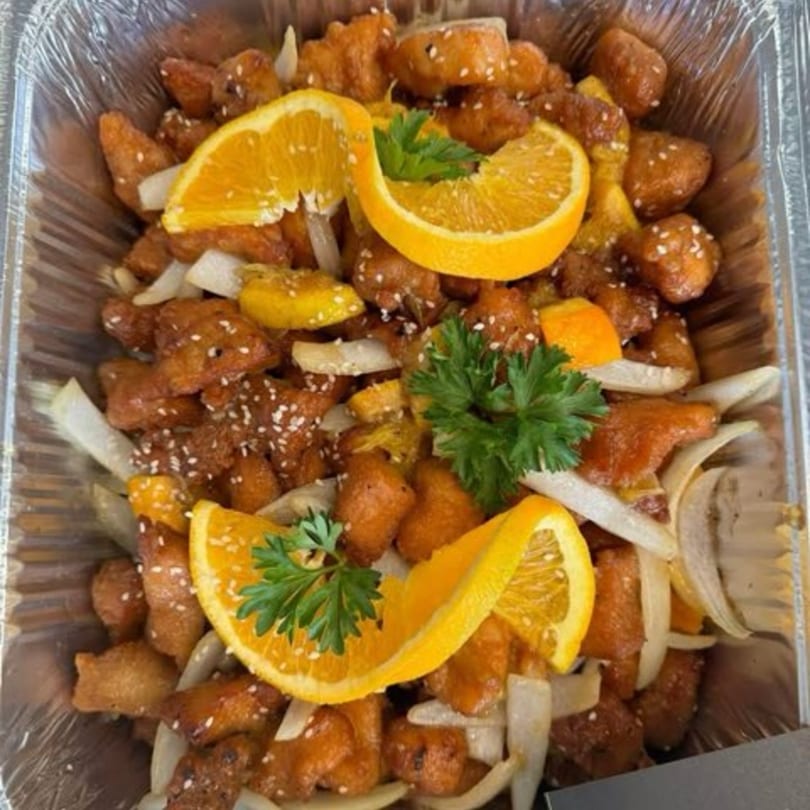 Delish Thai Kitchen's orange chicken with sesame seeds, onions, orange slices, and parsley in a foil container.