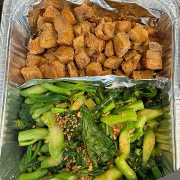 A foil container holds crispy pork belly and stir-fried Chinese broccoli from Delish Thai Kitchen.