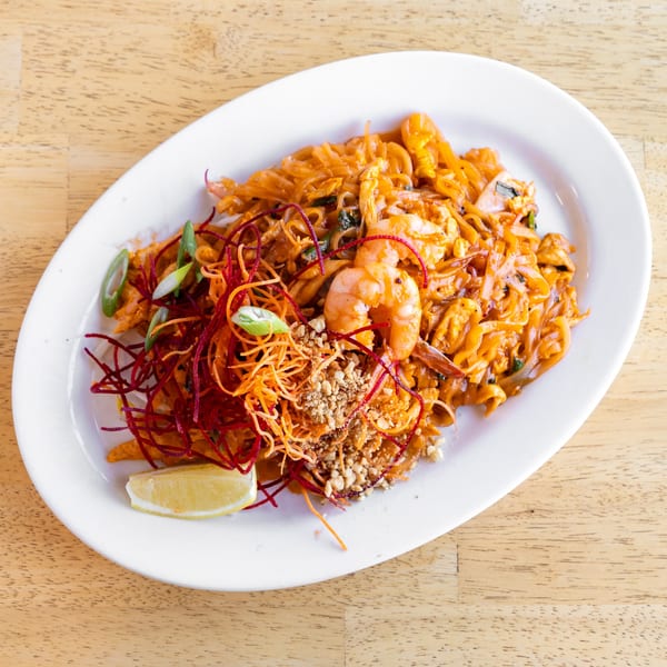 Delish Thai Kitchen's Pad See Ew with shrimp, shredded carrots, green onions, and a lemon wedge.