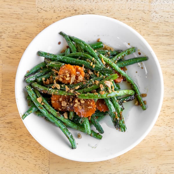Sautéed green beans and sliced carrots topped with crispy fried garlic on a white plate.