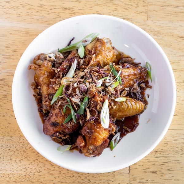 Delish Thai Kitchen's chicken wings in a dark sauce, topped with crispy fried shallots and scallions.