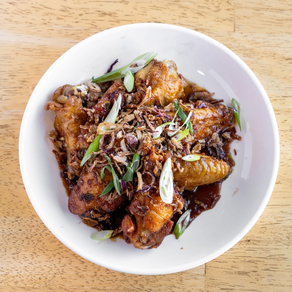 Delish Thai Kitchen's chicken wings in a dark sauce, topped with crispy fried shallots and scallions.