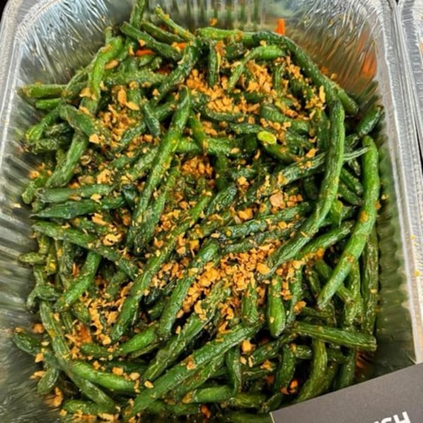 Delish Thai Kitchen's green beans, stir-fried and topped with crispy garlic, in a foil container.