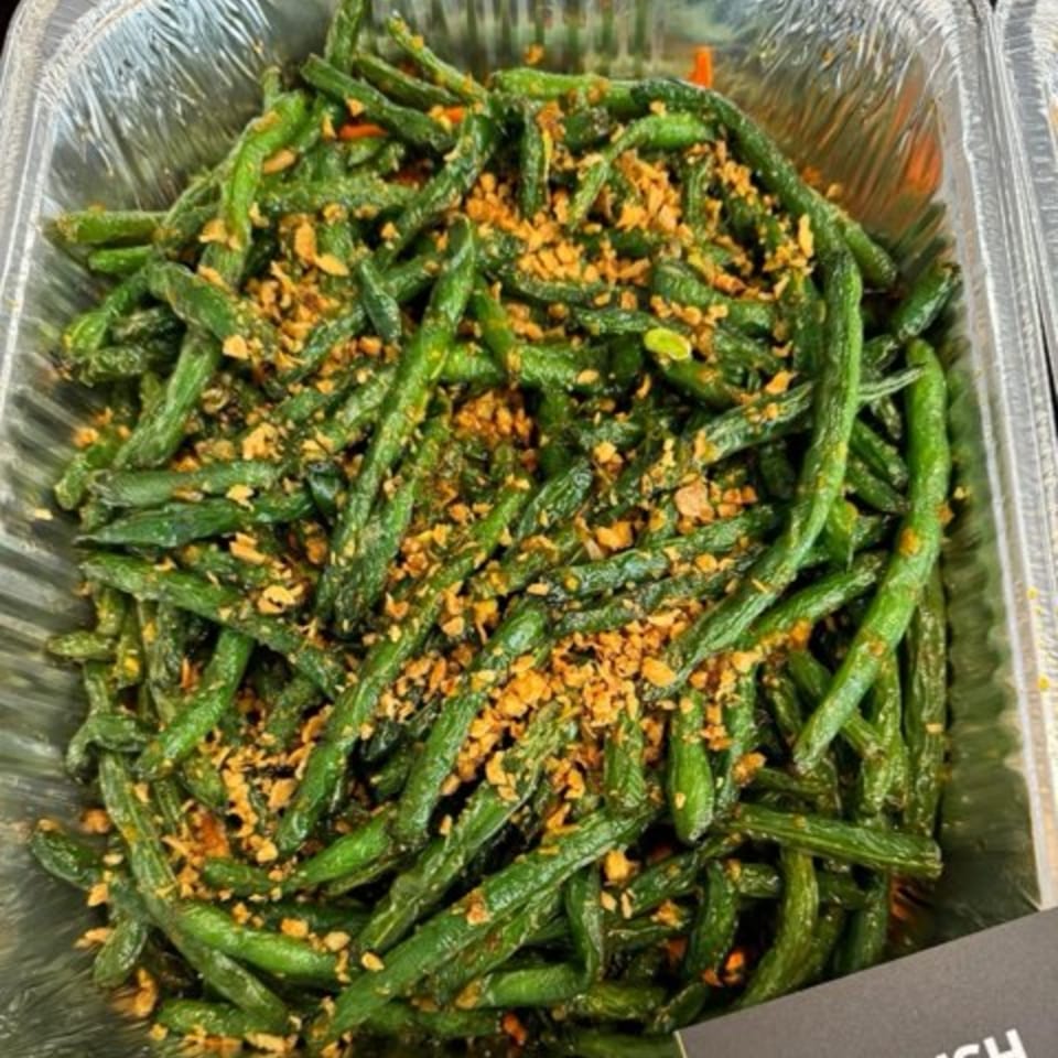 Delish Thai Kitchen's green beans, stir-fried and topped with crispy garlic, in a foil container.