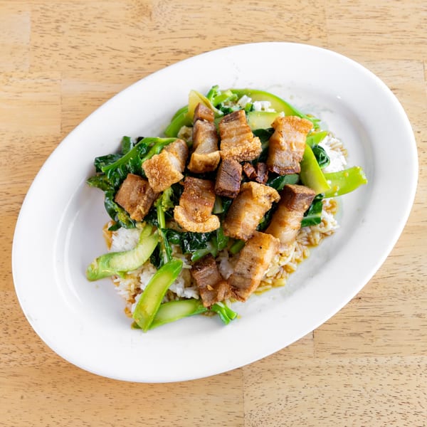 Crispy pork belly and Chinese broccoli stir-fry over rice, a popular Thai dish, on a white plate.