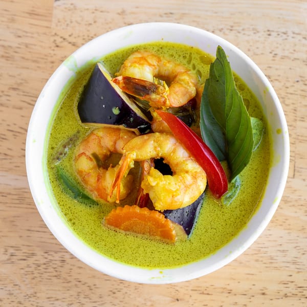 Delish Thai Kitchen's green curry with shrimp, eggplant, carrots, red chili, and basil in a white bowl.